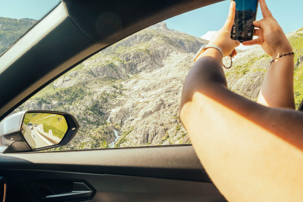 Person fotografiert eine Berglandschaft aus dem Auto während einer Fahrt mit dem Auto Abo von Arval