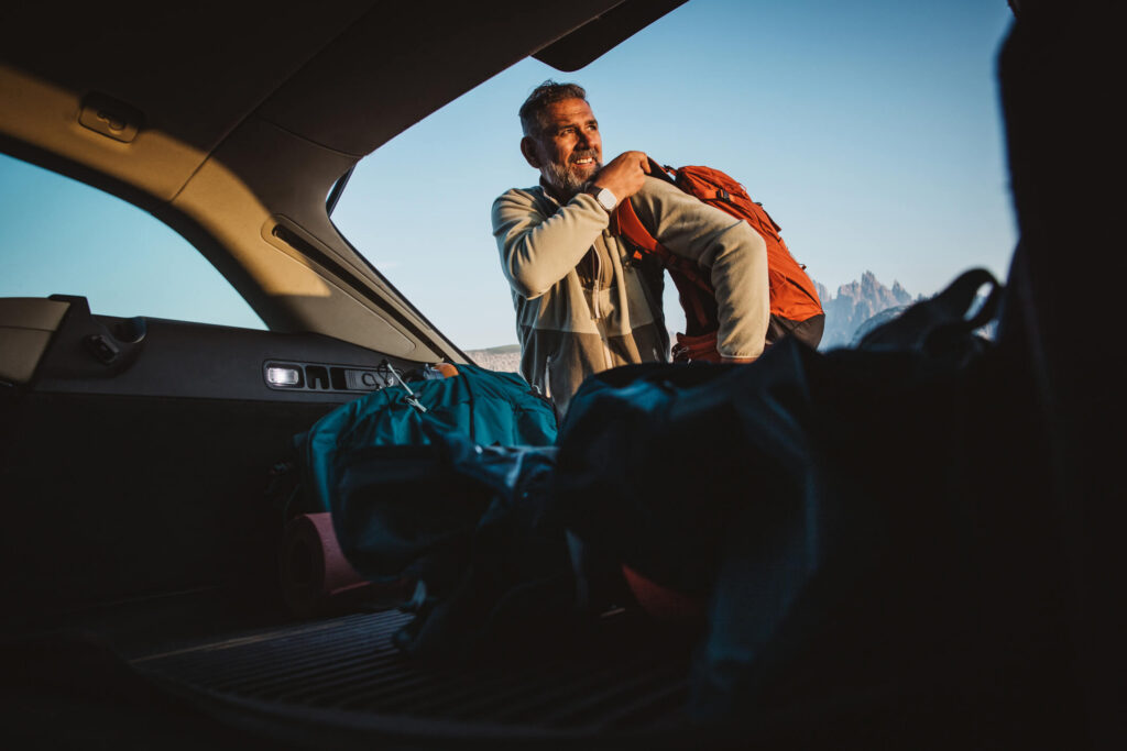 Mann mit Rucksack steht neben seinem Auto vor einer Wanderung mit dem Auto Abo von Arval